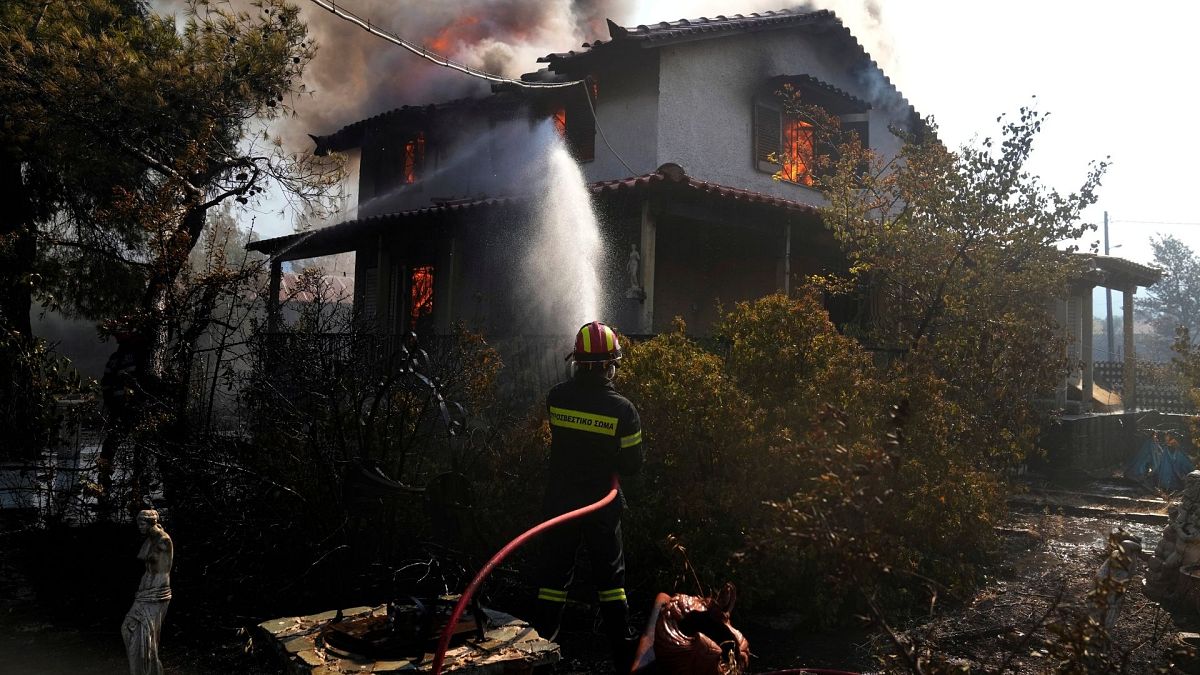A firefighter tries to extinguish the flames at a burning house 60 kilometers northwest of Athens, Greece