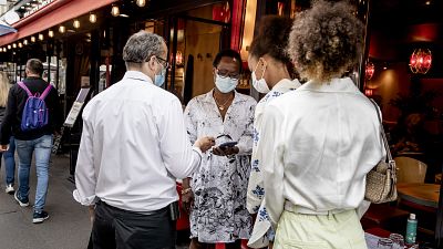 Women show their health passes to a waiter in Paris, Thursday, Aug. 19, 2021.