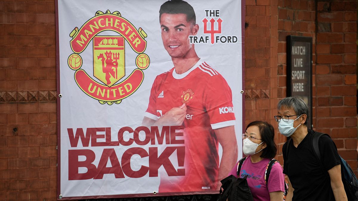 Fans walk past a banner featuring Manchester United's new signing Cristiano Ronaldo at Old Trafford stadium.