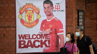 Fans walk past a banner featuring Manchester United's new signing Cristiano Ronaldo at Old Trafford stadium.