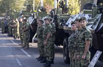 Serbian army soldiers stand to attention in front of armored personnel carriers in Belgrade.