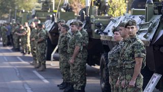 Serbian army soldiers stand to attention in front of armored personnel carriers in Belgrade.