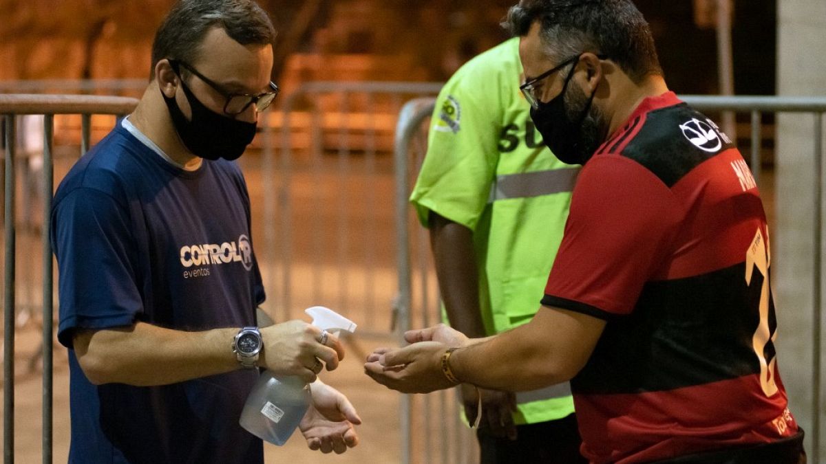 Adepto desinfeta mãos à entrada do Estádio do Maracanã, Rio de Janeiro