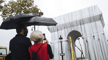 People watch workers wrapping the Arc de Triomphe ahead of the three-week installation on Wednesday