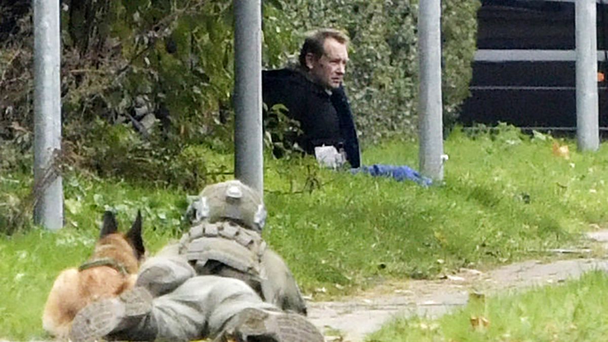 A police office watches Peter Madsen as he sits on the side of a road after being apprehended following a failed escape attempt in Albertslund, Denmark, Oct. 20, 2020.