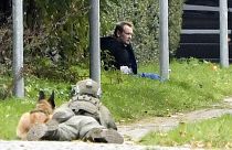 A police office watches Peter Madsen as he sits on the side of a road after being apprehended following a failed escape attempt in Albertslund, Denmark, Oct. 20, 2020.