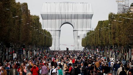 Pedestrians walking along the Champs-Elysees, in front of the Arc de Triomphe wrapped in silver by the late artist Christo.
