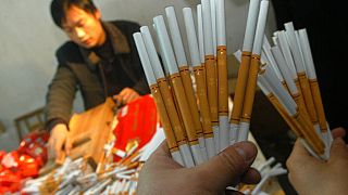 A shop worker, background, arranges fake cigarettes as officers of the Chengdu Tobacco Administration displays confiscated cigarettes at a counterfeiting shop in Chengdu.
