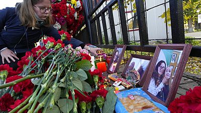 A student places a candle next to flowers and portraits of victims of shooting, outside the Perm State University following a campus shooting in Perm.