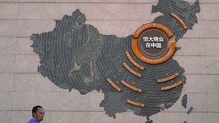 A custodian stands near a map showing Evergrande development projects in China on a wall in an Evergrande city plaza in Beijing, Tuesday, September 21, 2021.