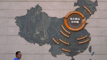A custodian stands near a map showing Evergrande development projects in China on a wall in an Evergrande city plaza in Beijing, Tuesday, September 21, 2021.
