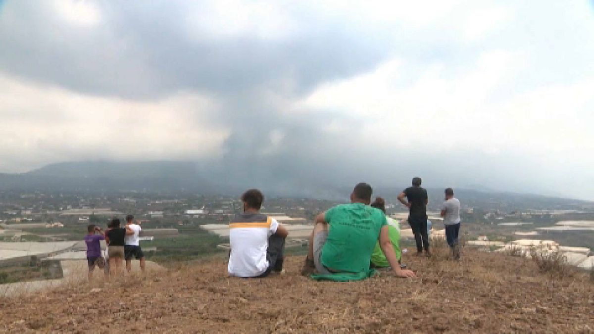 Habitantes evacuados de la isla de la Palma contemplan en la distancia como la lava destruye sus hogares