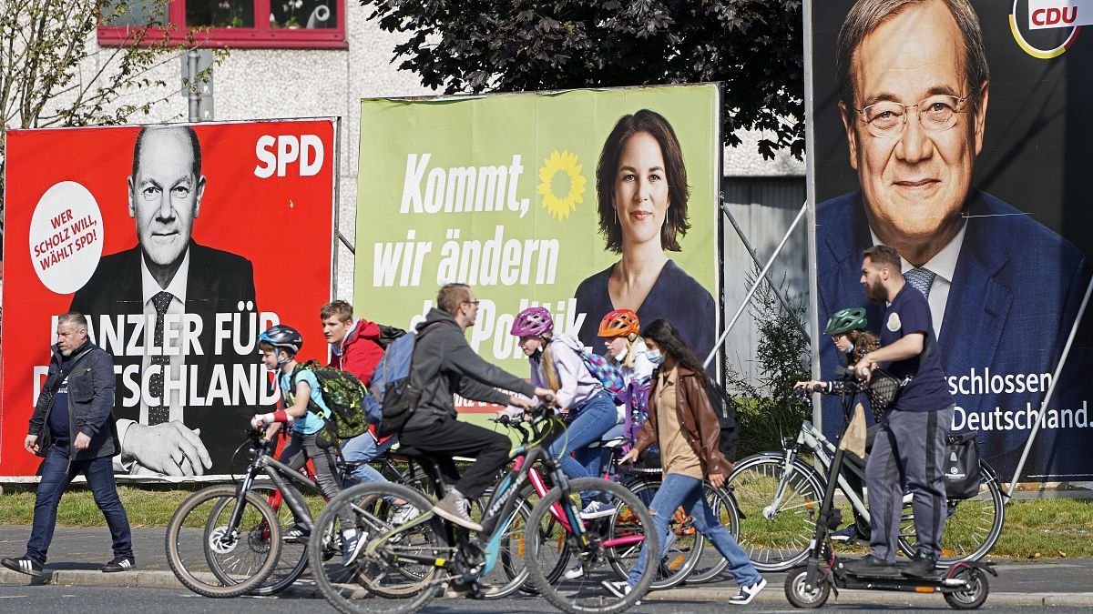 People walk and drive past election posters of the three German chancellor candidates.