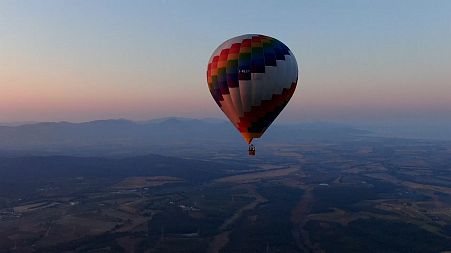 A hot air balloon soars above the Tuscan countryside