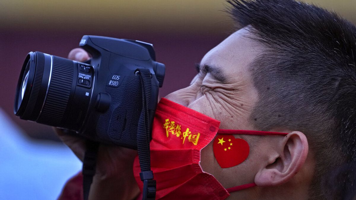 Un hombre luce una mascarilla con el lema "amo China" mientras fotografía el izado de bandera. Pekín, China 1/10/2021