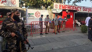 A Taliban fighter (L) stands guard as Afghan medical staff members wait at the entrance of a hospital to receive the victims of an explosion in Kabul on October 3, 2021.