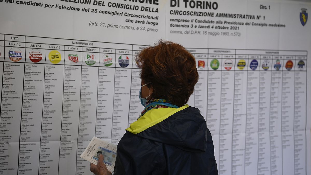 امرأة تنظر إلى أسماء المرشحين وشعارات الحزب في مركز اقتراع في تورينو بإيطاليا.