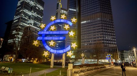 In this Thursday, March 11, 2021 file photo, a man walks past the Euro sculpture in Frankfurt, Germany.