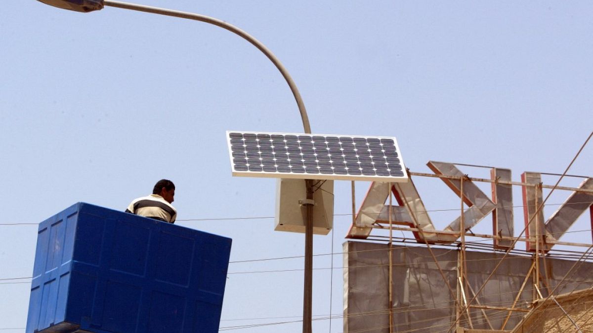 صورة من تلارشيف -  تعديل لوح شمسي متصل بأعلى عمود كهرباء على طريق رئيسي في منطقة الكرادة ببغداد