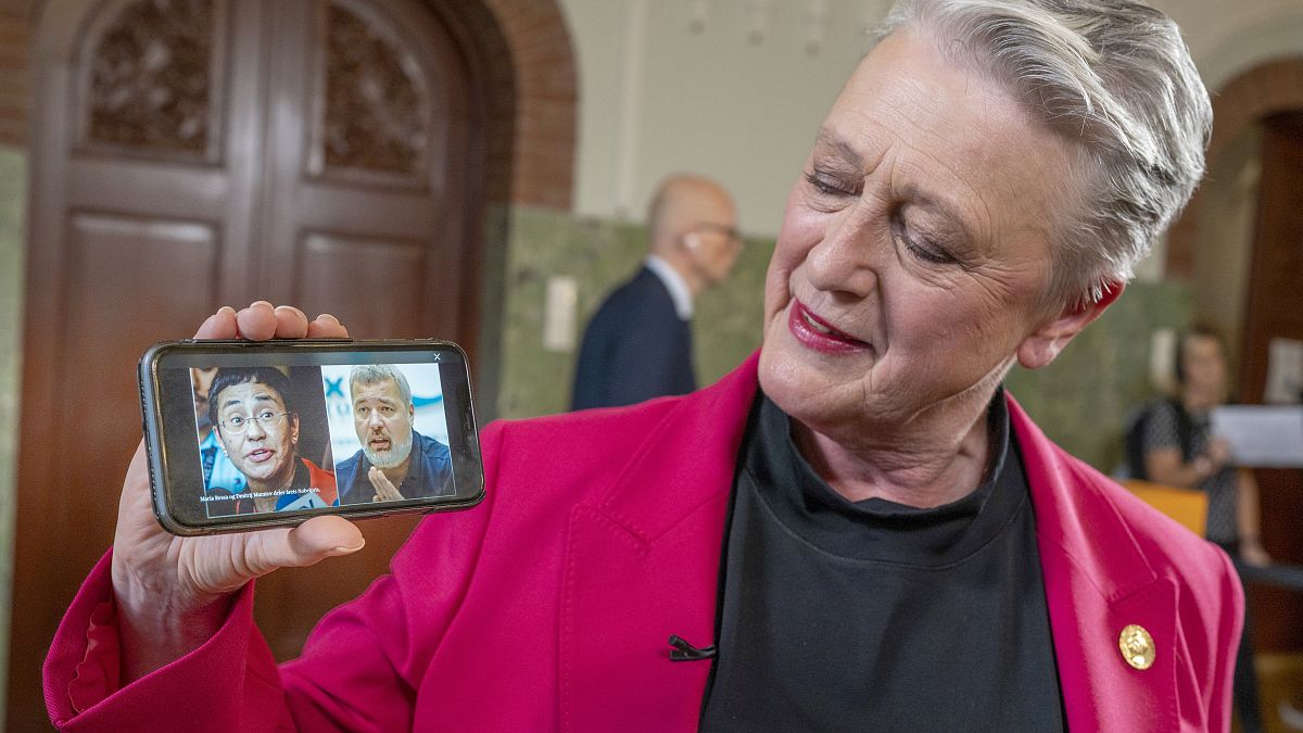 Берит Рейсс-Андерсен держит смартфон, на экране которого фотографии лауреатов Нобелевской премии мира этого года