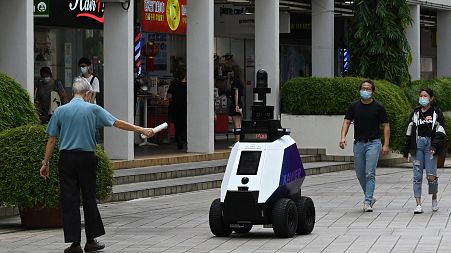A man gestures to an autonomous robot named "Xavier" as it patrols a shopping and residential district in Singapore.