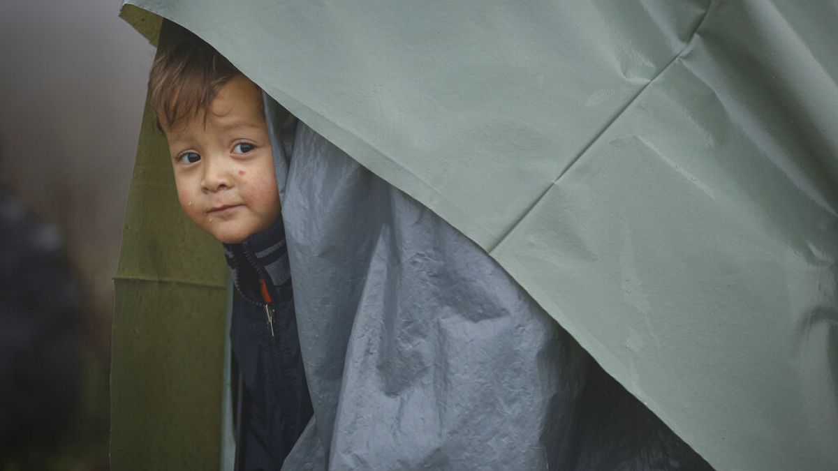 A migrant child peers from a makeshift tent at a camp housing migrants mostly from Afghanistan in Velika Kladusa, Bosnia, Tuesday, Oct. 12, 2021. 