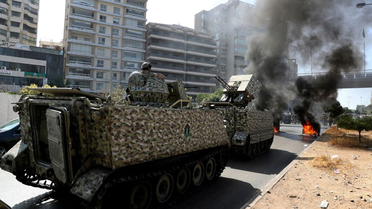 Lebanese army soldiers stand guard protesters burn garbage containers to block a road in Beirut.