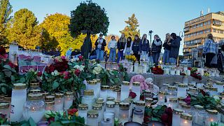 Young people look at the floral tributes and candles left for the victims of a bow and arrow attack, on Stortorvet in Kongsberg, Norway, Friday, Oct. 15, 2021.