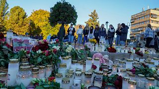 Young people look at the floral tributes and candles left for the victims of a bow and arrow attack, on Stortorvet in Kongsberg, Norway, Friday, Oct. 15, 2021. 