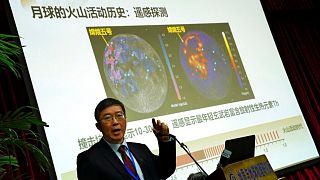 Li Xianhua speaks near a screen showing the volcano activities on the moon