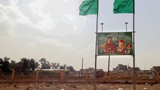 صورة تظهر لافتة  لمعمر القذافي وعلم من عهد القذافي في مدينة بني وليد، ليبيا.