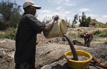 عامل يسكب وعاء  من الماء المليء بالتربة في وعاء بلاستيكي أصفر أثناء تعدين الذهب غير القانوني في رودبورت، جنوب إفريقيا.