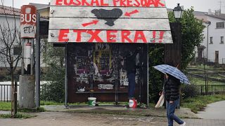 Une femme passe devant un arrêt de bus sur lequel on peut lire en basque "ETA" à gauche et "Prisonniers basques, rentrez chez vous"