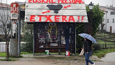 A woman walks past a public bus stop that reads in Basque: ''ETA'' on the left, and ''Basque prisoners, go home''.
