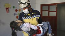 Un casco blanco de la Defensa Civil siria lleva en brazos a una niña herida en el bombardeo