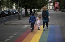 A woman and children walk on a pedestrian crossing painted in the colours of the rainbow flag, a symbol of the gay rights movement in Vilnius, Lithuania.