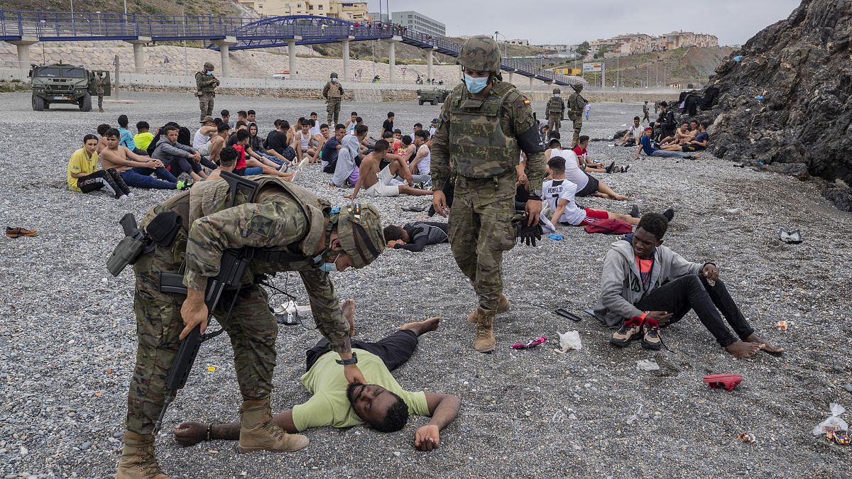 Солдаты армии Испании и группа нелегальных мигрантов в полуэкславе Сеута на границе с Марокко 