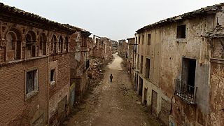 A tourist guide walks down the central street through the ruins of Belchite village.