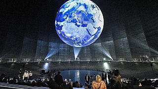 Los visitantes observan un globo terráqueo en la exposición "The Fragile Paradise" durante la COP26