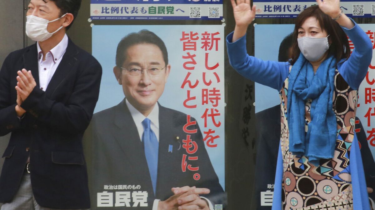 A supporter of Japan's governing Liberal Democratic Party waves by posters of the party president, Japanese Prime Minister Fumio Kishida, Tokyo, Wednesday, Oct. 27, 2021. 