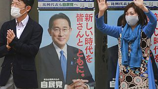 A supporter of Japan's governing Liberal Democratic Party waves by posters of the party president, Japanese Prime Minister Fumio Kishida, Tokyo, Wednesday, Oct. 27, 2021. 