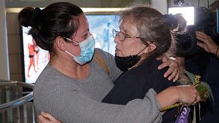 A woman, right, is embraced by a loved-one after arriving on a flight from Los Angeles at Sydney Airport.