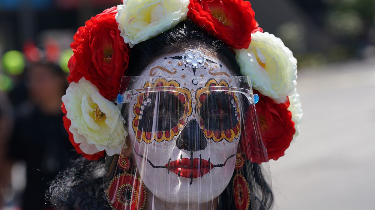 Una mujer disfrazada de "Catrina" y con una pantalla facial posa para una foto durante las festividades del Día de Muertos en la Ciudad de México, el 31 de octubre de 2021.