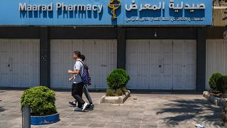 أشخاص يمرون أمام الباب المغلق لصيدلية في مدينة طرابلس شمال لبنان، خلال إضراب على مستوى البلاد للصيدليات احتجاجا على النقص الحاد في الأدوية، في 9 يوليو / تموز 2021.