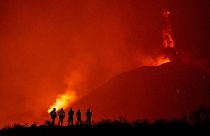 Police officers and emergency personnel look as lava flows from the Cumbre Vieja volcano.
