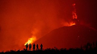 Police officers and emergency personnel look as lava flows from the Cumbre Vieja volcano.