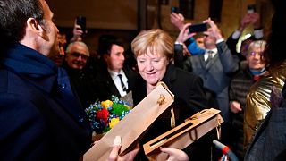 German Chancellor Angela Merkel and French President Emmanuel Macron, left, receive flowers and a bottle of wine as gifts as they are greeted by residents in Beaune, Burgundy,