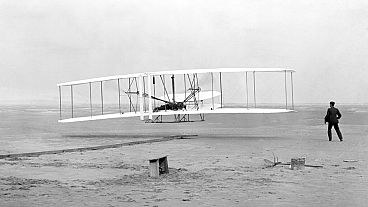 أورفيل رايت، مستلقياً على أدوات التحكم في الجناح السفلي، يقود طائرة رايت فلاير في أول رحلة تعمل بالطاقة بواسطة طائرة أثقل من الهواء، 17 كانون الأول / ديسمبر 1903
