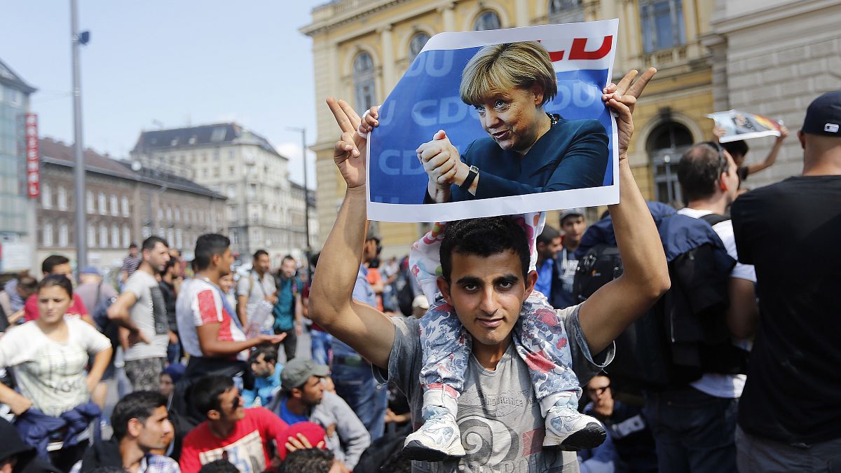 FILE - A migrant holds up a poster of German Chancellor Angela Merkel before starting a march out of Budapest, Hungary, towards Austria and Germany, Sept. 4, 2015