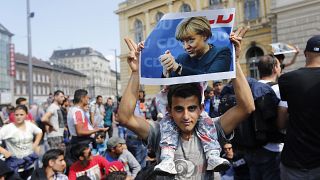 مهاجر يحمل ملصقًا للمستشارة الألمانية أنغيلا ميركل قبل انطلاق مسيرة من بودابست عاصمة المجر، نحو النمسا. 2015/09/04
